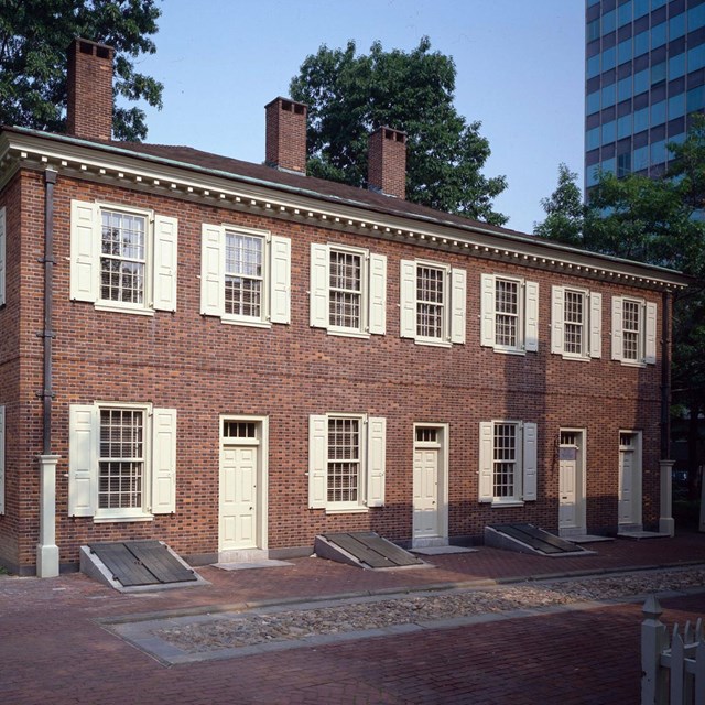 Color photo of a narrow two story red brick building with rows of windows on both floors.