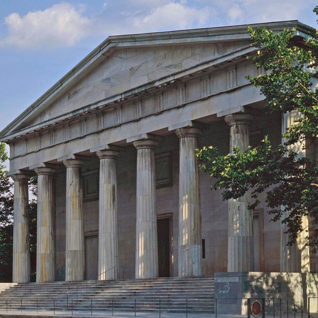 Color photo of a large classical looking building with marble columns below a triangular pediment.