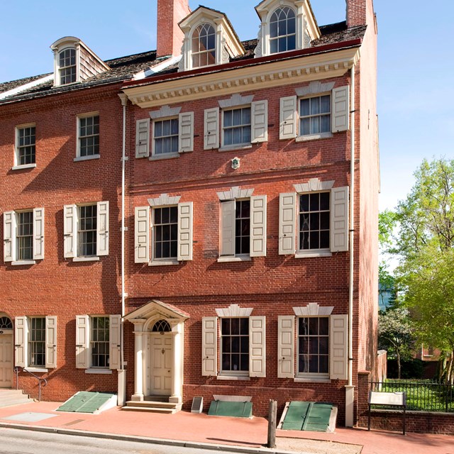 Color photo of a three story red brick rowhouse at the end of the row.
