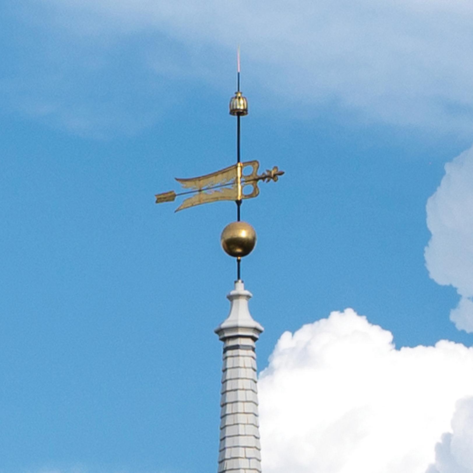 Gold weathervane with a blue sky and clouds in the background.