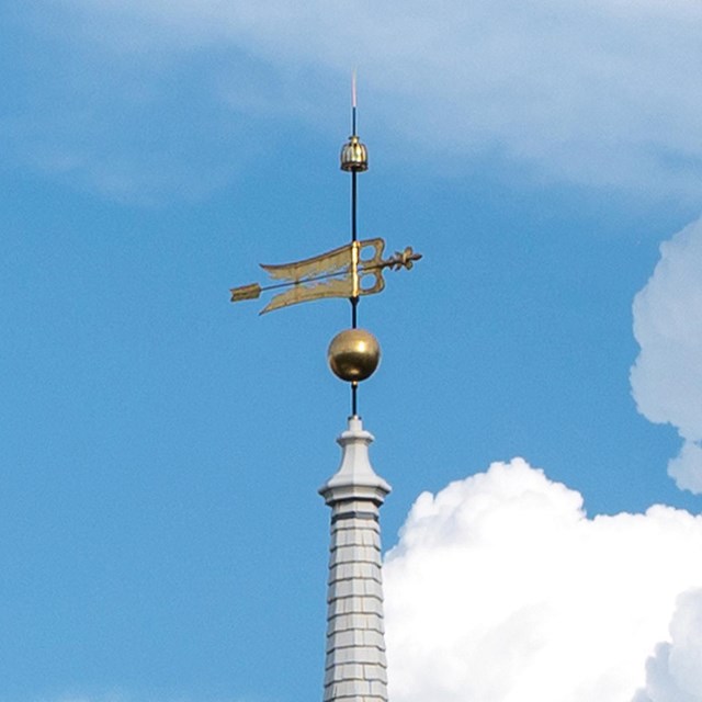 Gold weathervane with a blue sky and clouds in the background.