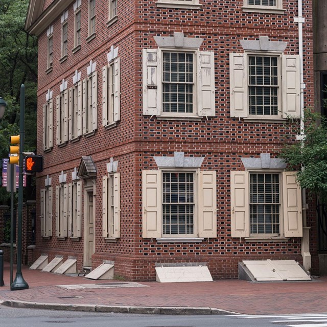 Color photo of a narrow, multi-story red brick house on a corner property