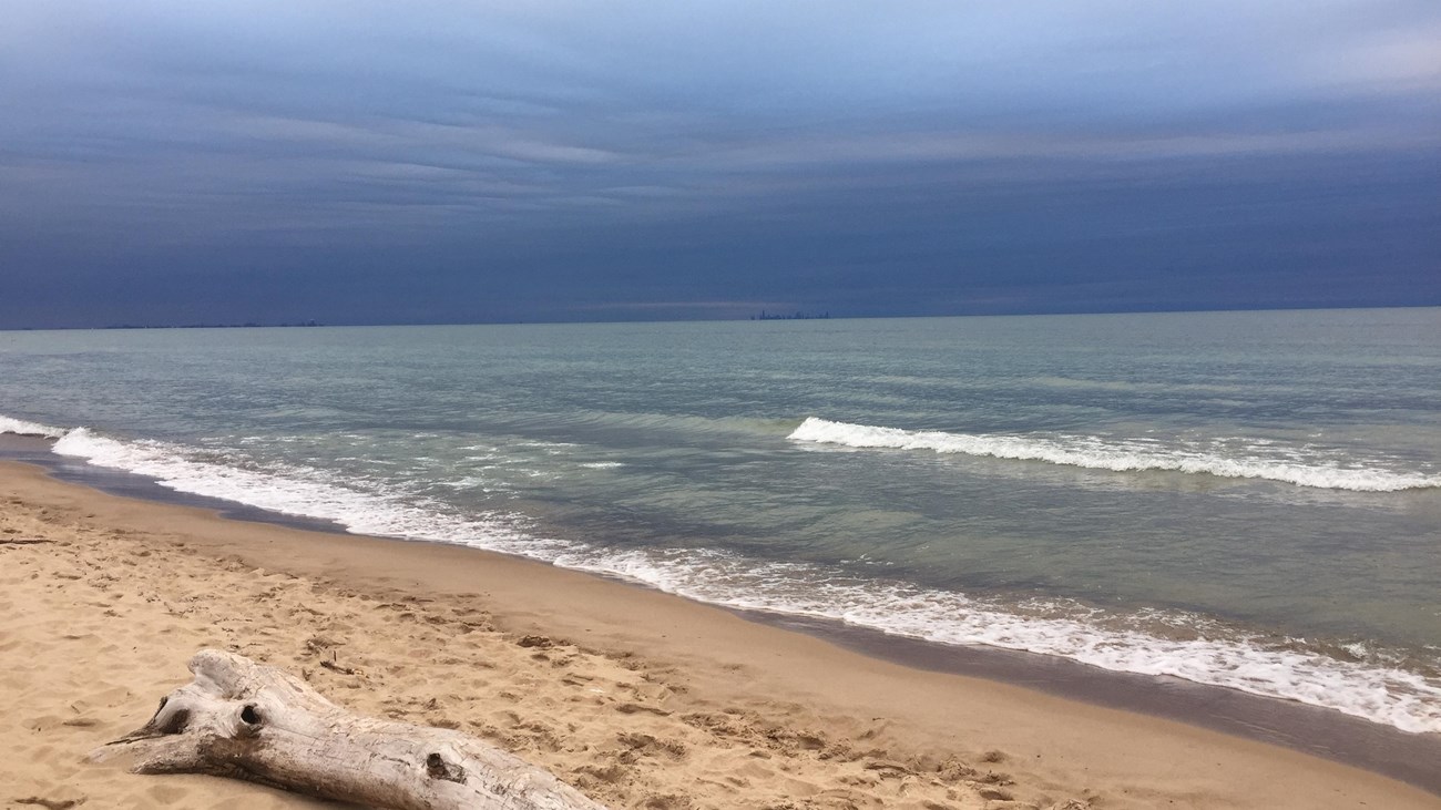 Lake Michigan's green/blue, gentle waves rolling onto a sandy beach with a washed ashore log. 