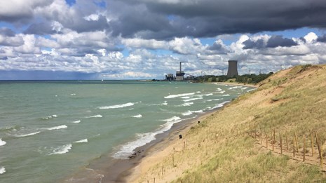 Grass covered dune overlooking a turbulent Lake Michigan with Michigan City's generating tower.  