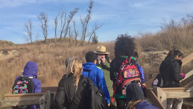 An NPS ranger speaks to a crowd of students on a boardwalk surrounded by dunes