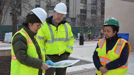 Three National Park Service employees in construction safety equipment looking over plans 