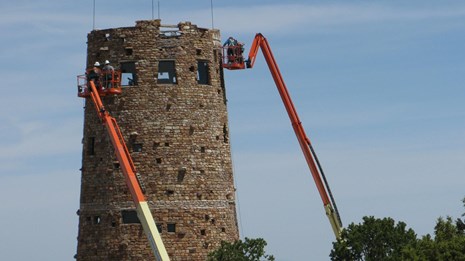 Elevated platform holding construction workers near the top of a historic stone tower