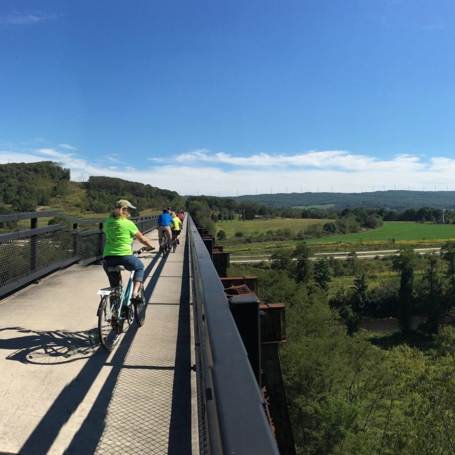 Bicyclists on a bridge overlooking a valley 