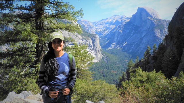 An International Volunteer stands on a hilltop with a stunning mountain behind her. 