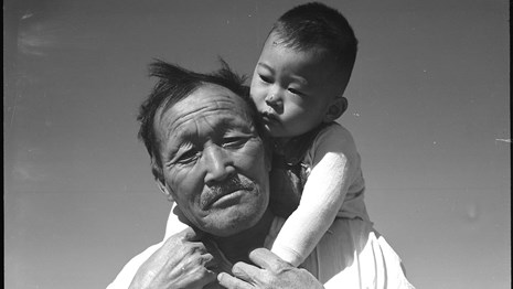 Older Japanese man holds a baby on his shoulders. 