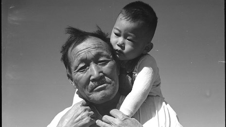 Older Japanese man holds a baby on his shoulders.