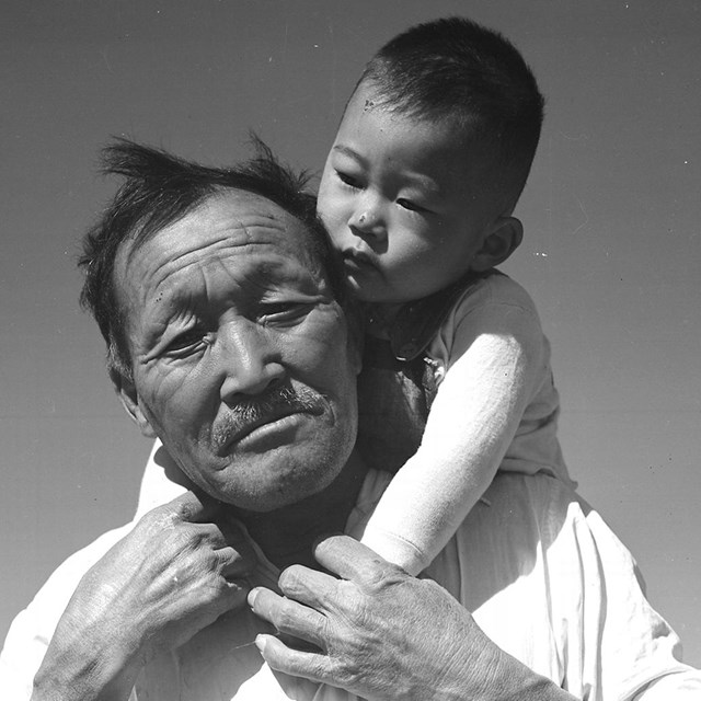 Older Japanese man holds a baby on his shoulders. 