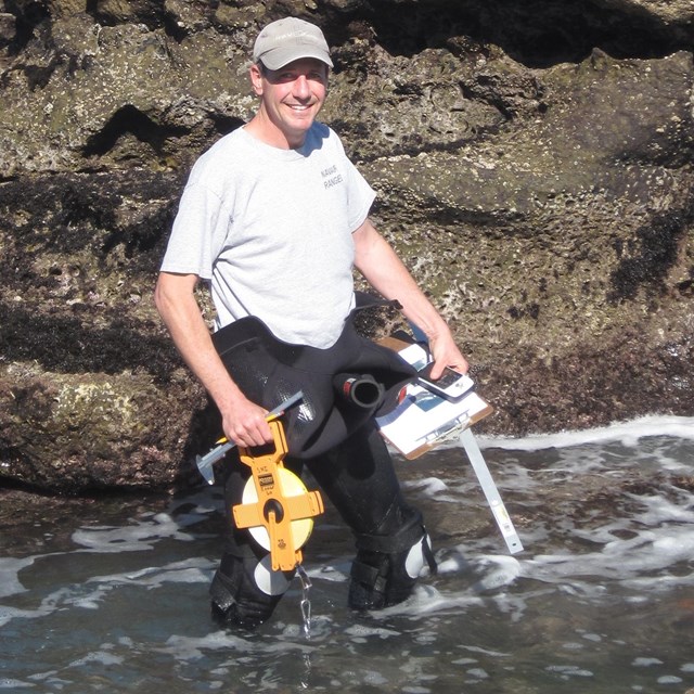 Man standing in tidepool with hat and tools.