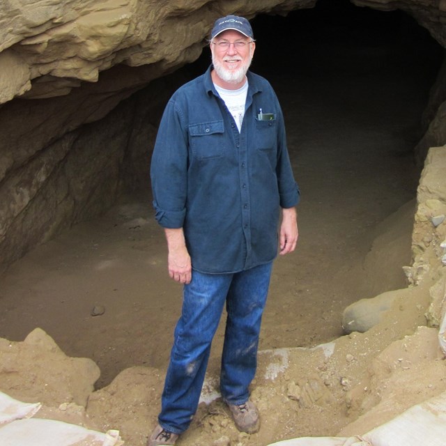 Man standing next to cave entrance. 