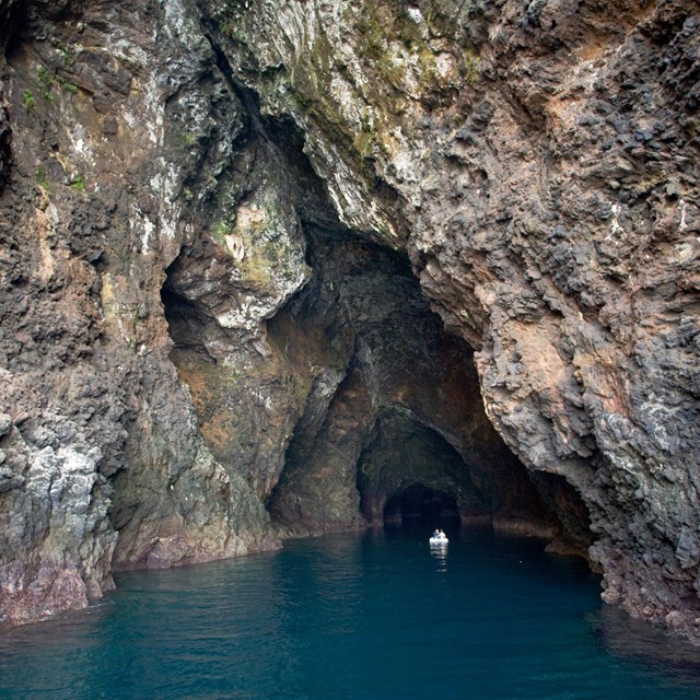 Sea cave with rust and black colored rocks and boat in the middle.