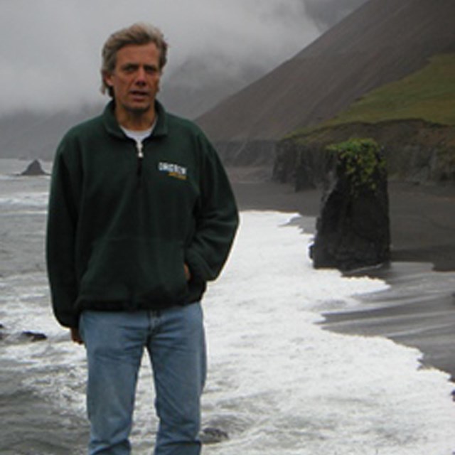 Man standing along coast with waves breaking. 