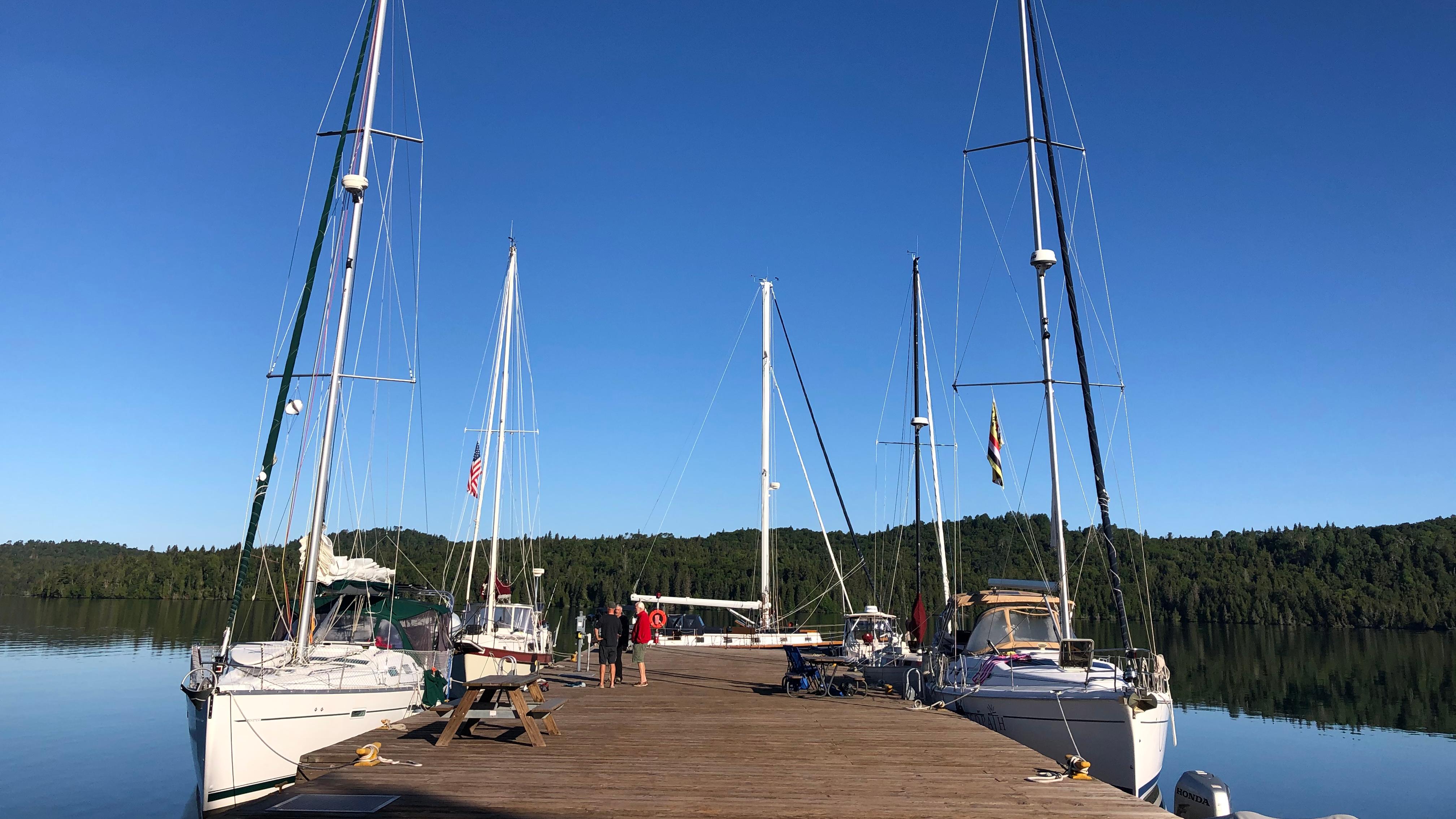 Multiple sailboats are docked around a large, wooden dock.