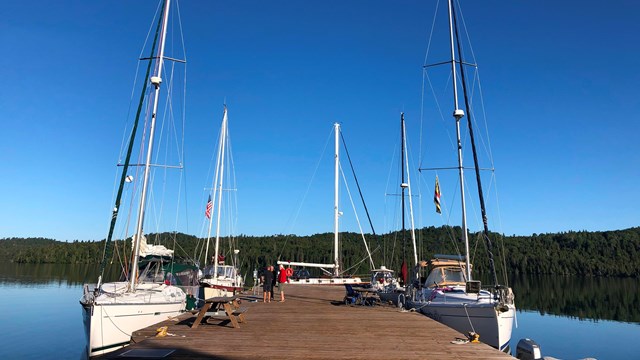 Multiple sailboats are docked around a large, wooden dock.