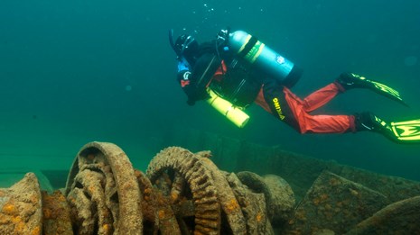 An underwater photo shows a scuba diver examining equipment on a shipwreck.