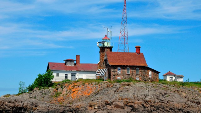 view of the rocky shoreline in the foreground of the Passage Island lighthouse, garage, and tower