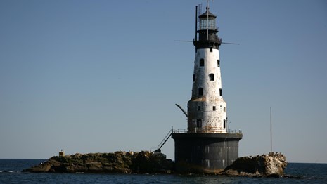 lighthouse standing on a desolate rocky reef on a blue sky day