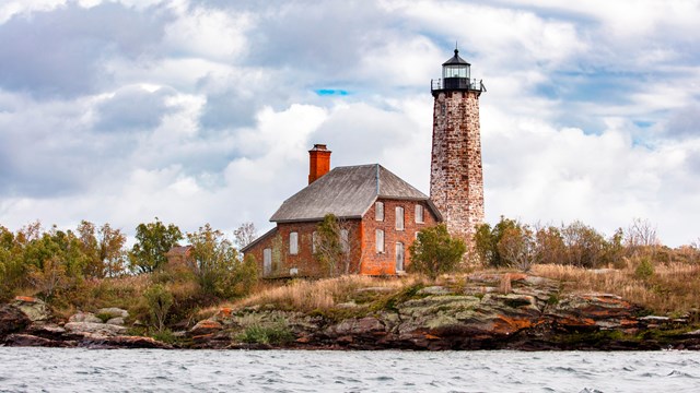 just a small piece of blue jetting through the clouds atop a lighthouse on a rocky island