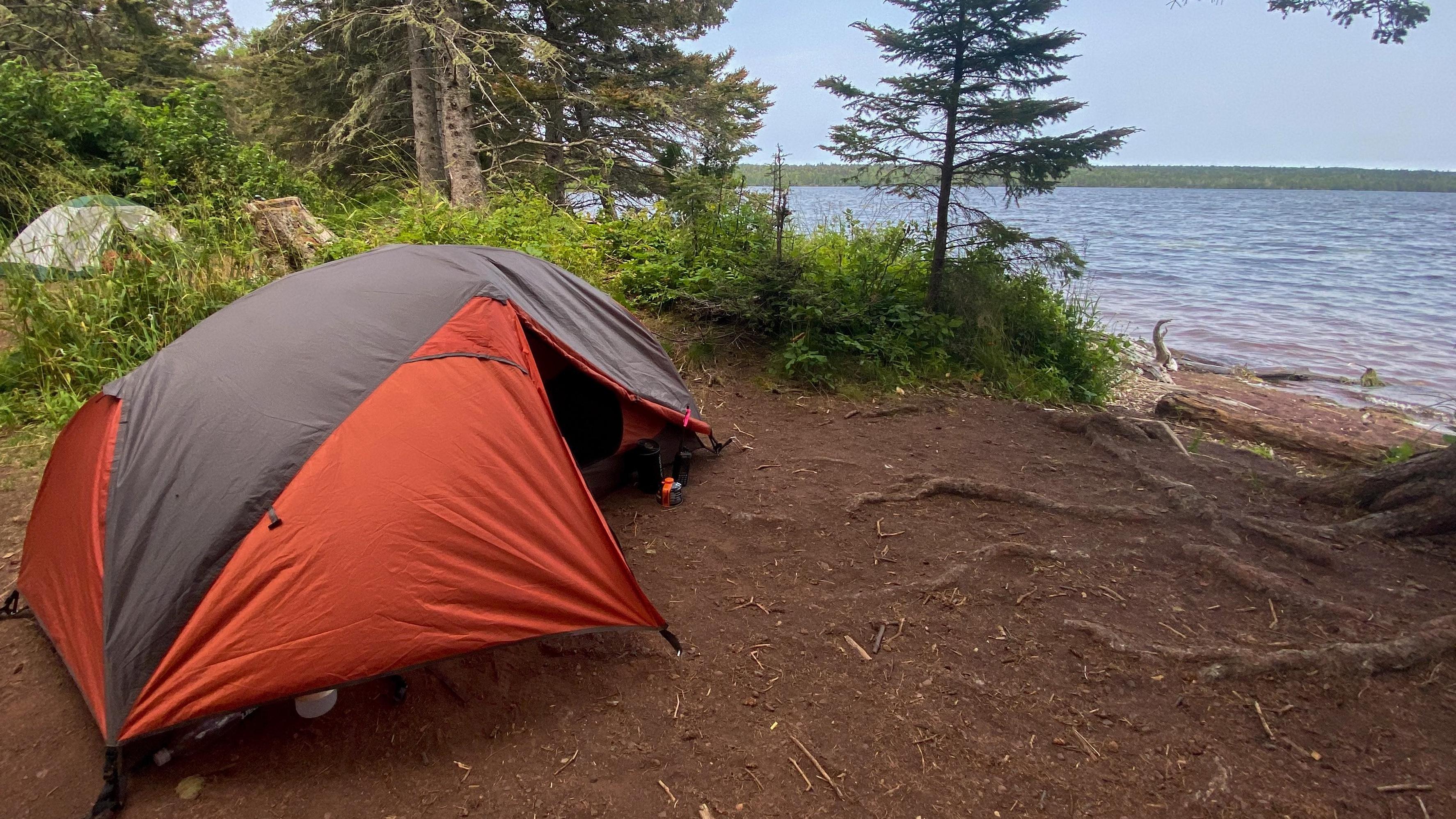 An orange tent sits at a wooded campsite facing Lake Superior. 