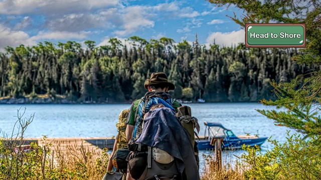 A hiker with a large backpack walking towards a lakeshore.