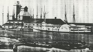 SS Cumberland docked in Collingswood, ON, large building in background logs in foreground