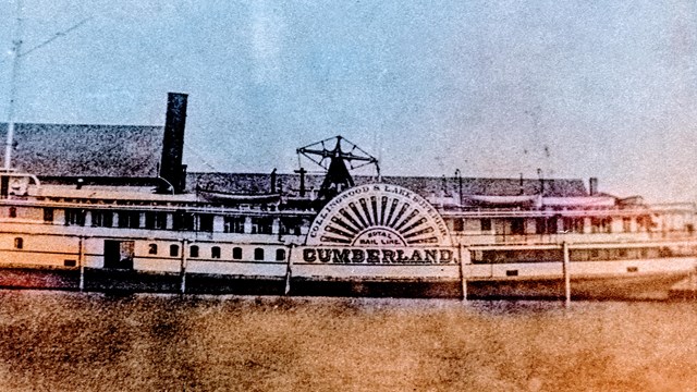 SS Cumberland docked with building behind it, sidewheel bearing name