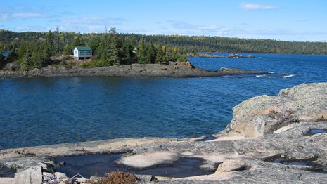 Cabin across a bay perched on the Lake Superior Shoreline. Splash pools on the rocky shoreline.