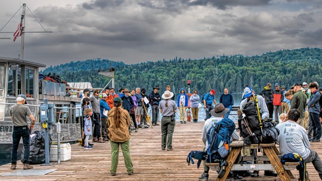 People gather around a park ranger on a dock.