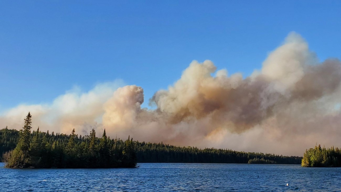 A view from the water of gray smoke billowing into the sky.