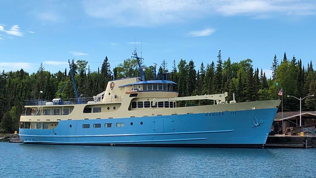 A large blue boat is shown at a dock with blue skies in the background.