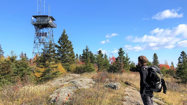 A hiker looks towards a tall fire lookout tower.
