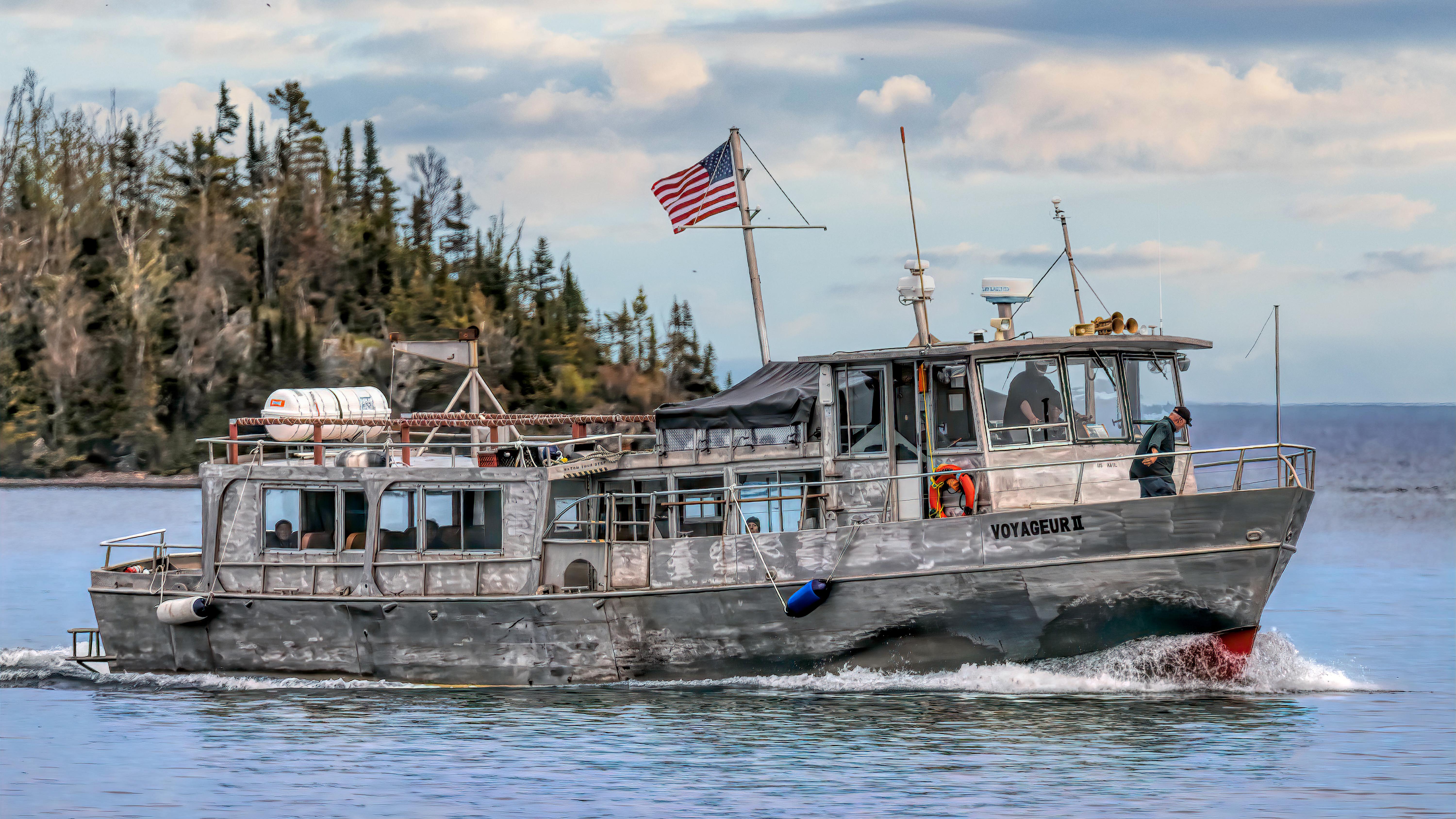 A large silver ferry boat sailing on a lake with an island in the background.