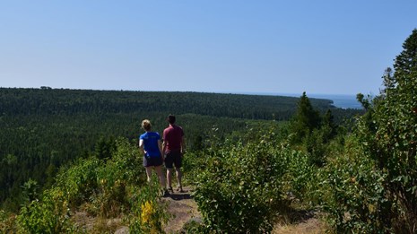 Two Hikers enjoy an overlook of the Isle Royale forest and the distant Lake Superior shoreline.