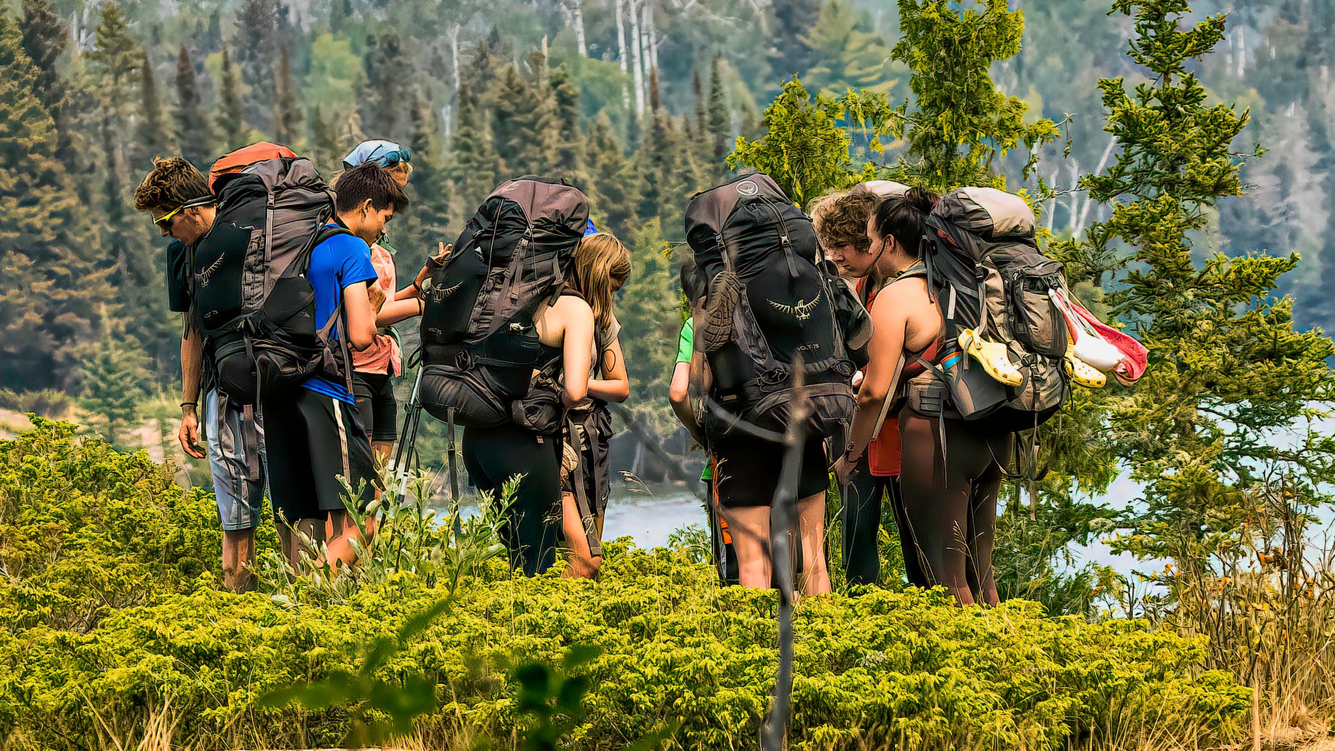A group of nine people with large backpacks and gear stand in a circle.