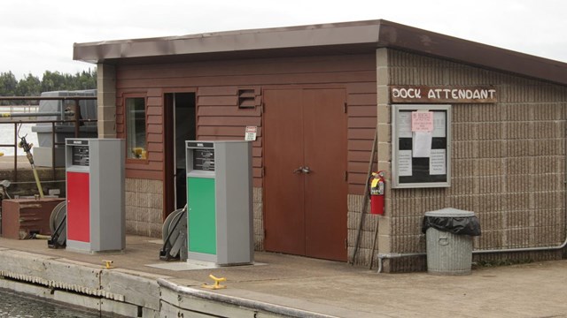 Two fuel pumps sit on a dock with a small building in the background