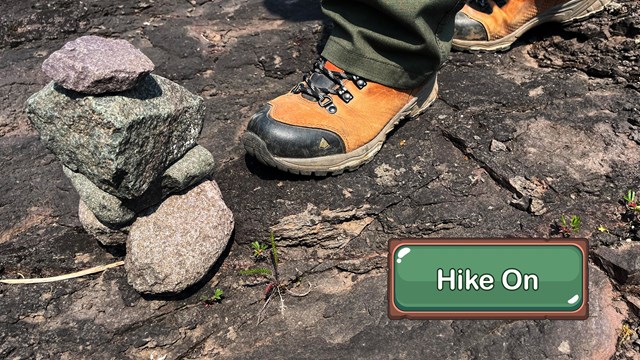 A close up of hiking boots walking by a stack of rocks.