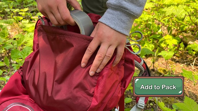 A person putting a roll of silver duct tape into their red backpack.