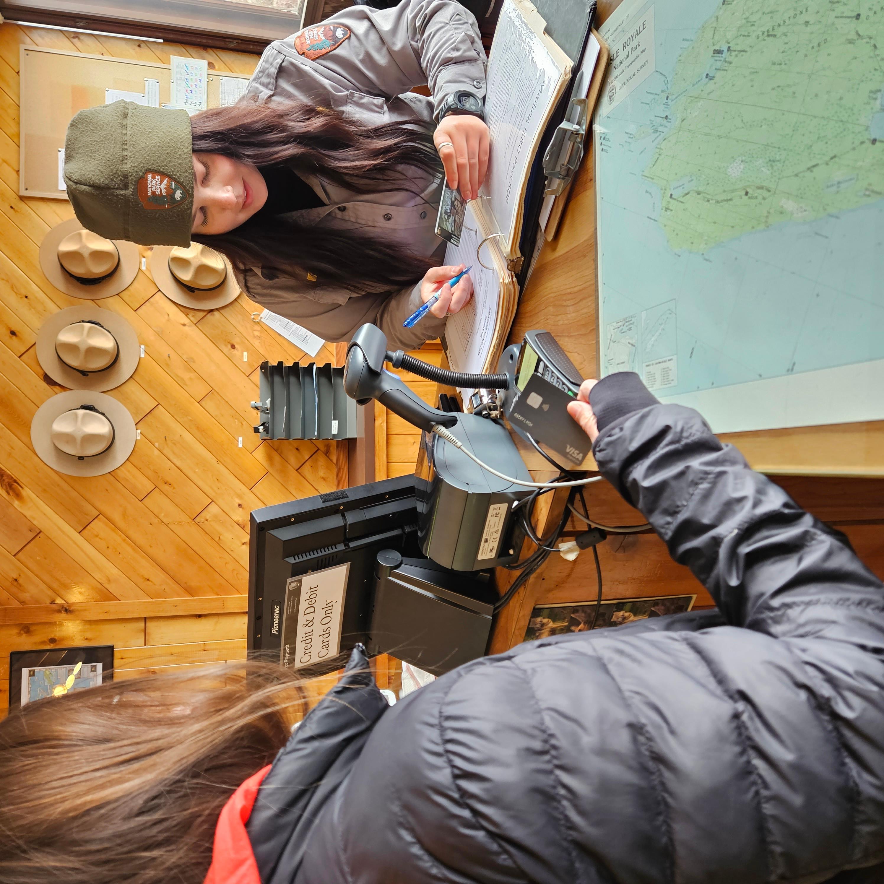 A park ranger at a desk selling a pass to a visitor. 