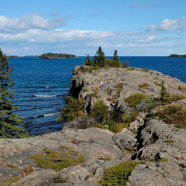 A rocky shore line covered in moss and lichen, looking out to smaller islands in Lake Superior.