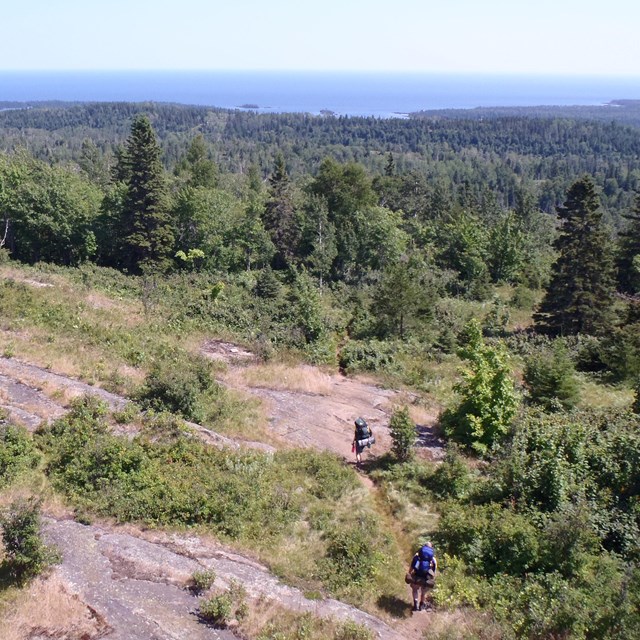 A rocky ridge overlooking two backpackers hiking through the ridge.