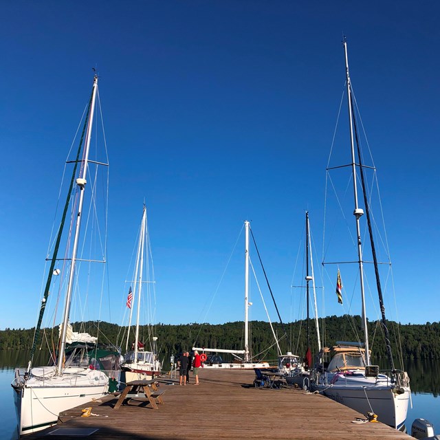 Multiple sailboats are docked around a large, wooden dock.