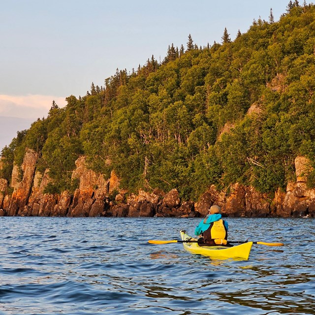 A kayaker paddles near the palisades during sunset on a clear day.