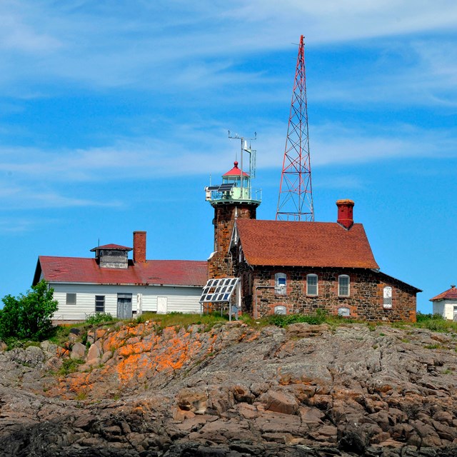 view of the rocky shoreline in the foreground of the Passage Island lighthouse, garage, and tower