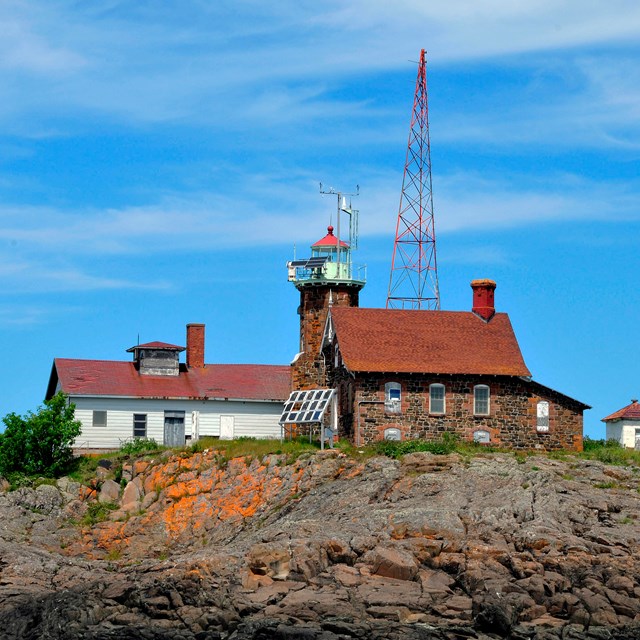 view of the rocky shoreline in the foreground of the Passage Island lighthouse, garage, and tower