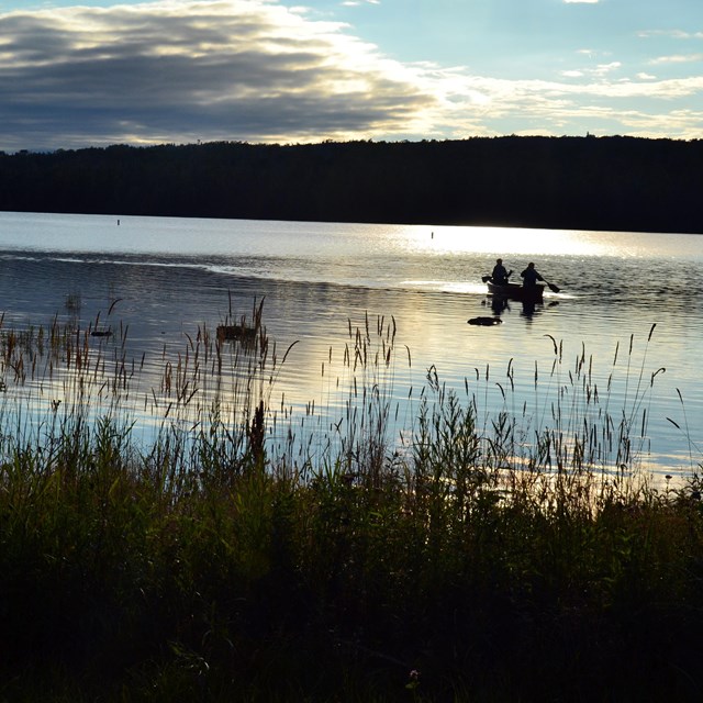 Two people paddling a canoe across calm waters at sunset.