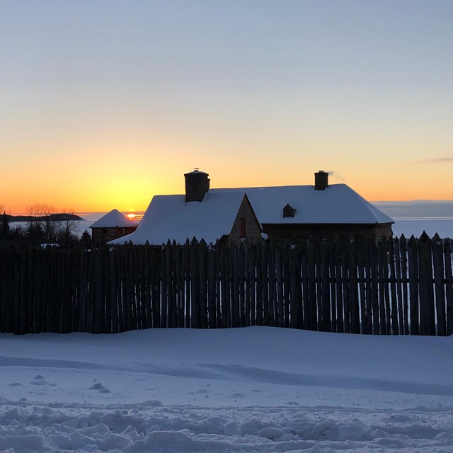 A sunset view of a building and fence in snow